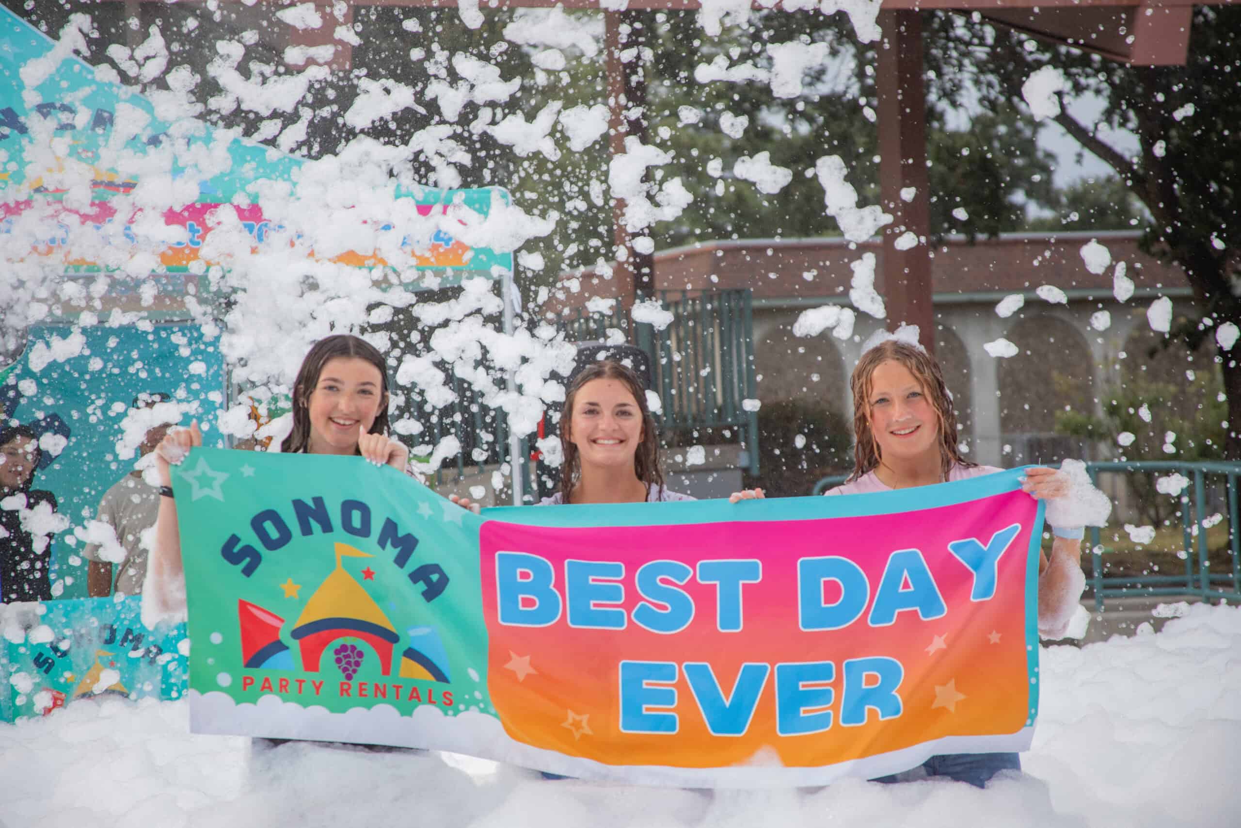 Three girls holding a Best Day Ever banner at a foam party rental